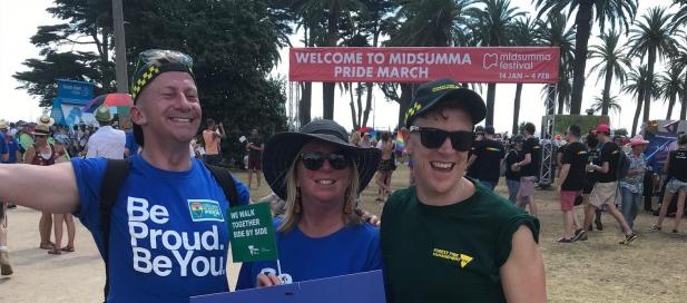 three people posing for a photo at the Midsumma Pride March. One of the people have a blue tshirt that says 'be proud, be you'