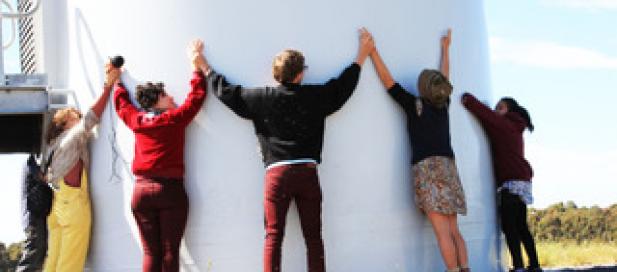five people hugging a large white cylinder outside