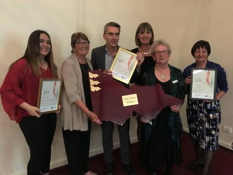 six people holding 4 awards between them, one shaped like the state of Victoria